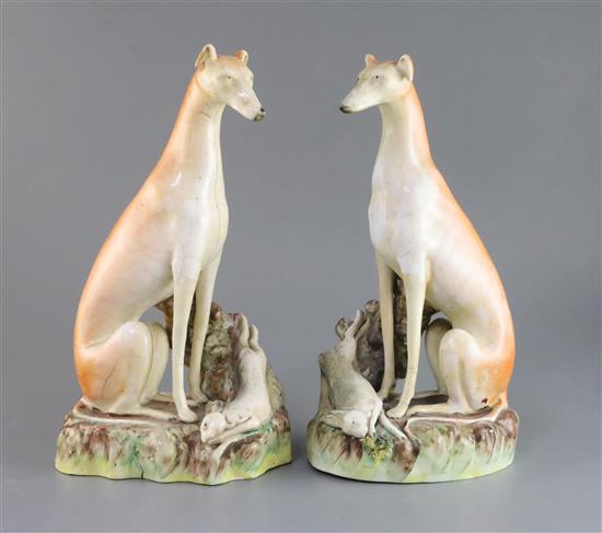 A pair of Victorian Staffordshire models of greyhounds seated with hares at their feet, 12.25in.